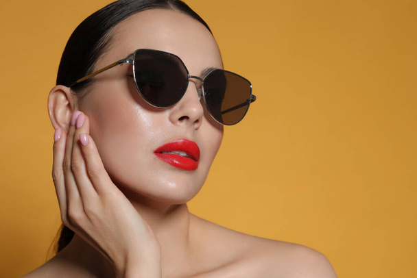 Attractive woman in fashionable sunglasses against orange background - Foto, Bild