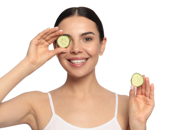 Beautiful young woman putting slices of cucumber on eyes against white background - Foto, imagen