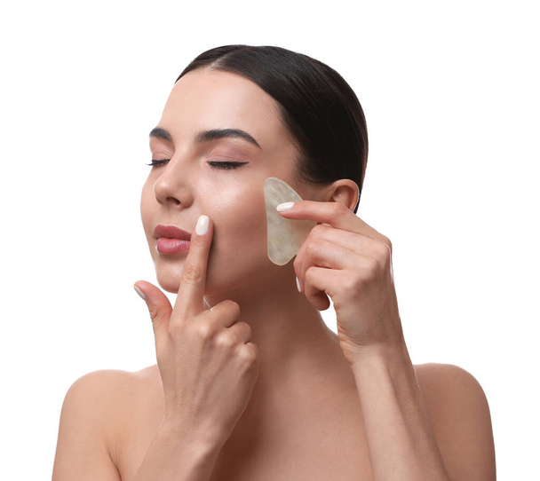 Beautiful young woman doing facial massage with gua sha tool on white background - Foto, afbeelding