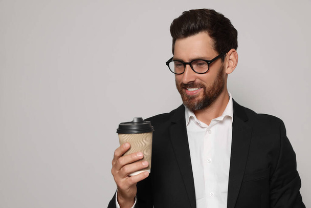 Handsome bearded man with glasses looking at paper cup on light grey background. Space for text - Фото, изображение