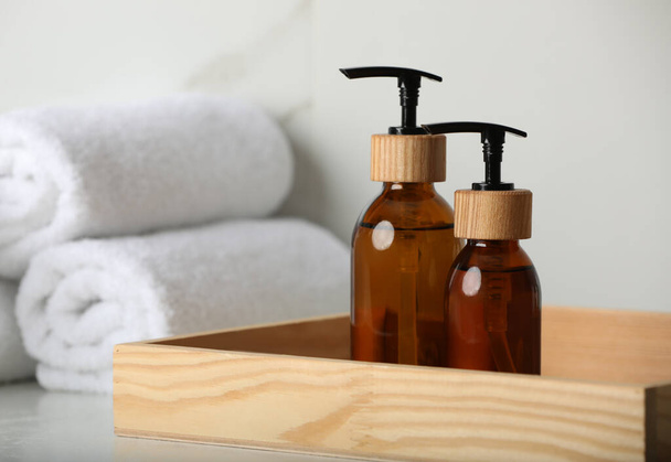 Wooden tray with dispenser bottles and towels on white table, closeup - Foto, Imagen