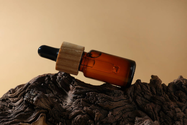 Bottle of essential oil on tree bark against dark beige background - Фото, изображение