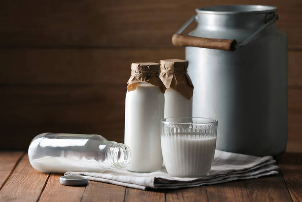 Tasty fresh milk in can, bottles and glass on wooden table, space for text - Zdjęcie, obraz