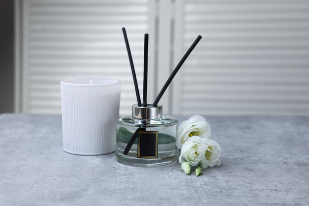 Reed diffuser, scented candle and eustoma flowers on gray marble table - Fotoğraf, Görsel