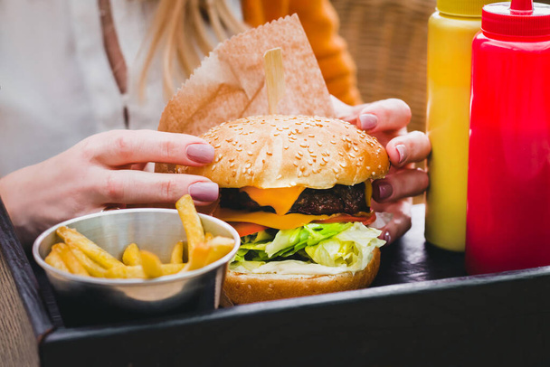Mains tenant un délicieux hamburger frais avec des frites sur la table en bois noir - Photo, image