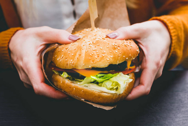 Mains féminines tenant un délicieux burger frais avec des frites sur la table en bois noir - Photo, image