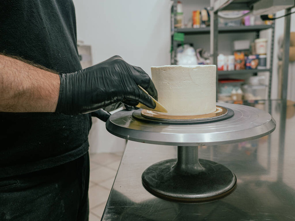 Décorateur utilisant spatule et grattoir pour lisser la crème au beurre sur un gâteau givré - Photo, image