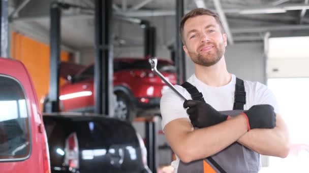 Portrét atraktivního usměvavého automobilového mechanika amerického vzhledu stojícího na pozadí automobilové dílny a držícího klíček od auta. Šťastný zaměstnanec - Záběry, video