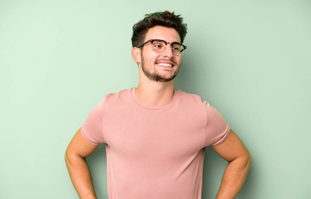 young handsome man looking happy, cheerful and confident, smiling proudly and looking to side with both hands on hips - Foto, Bild