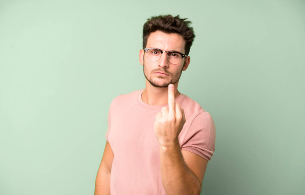 young handsome man feeling angry, annoyed, rebellious and aggressive, flipping the middle finger, fighting back - Photo, Image
