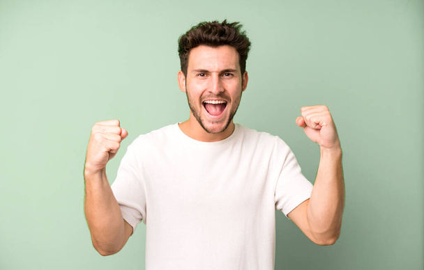young handsome man feeling happy, surprised and proud, shouting and celebrating success with a big smile - Fotoğraf, Görsel