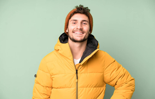 handsome teenager smiling happily with a hand on hip and confident. winter clothes and cold concept - Фото, изображение
