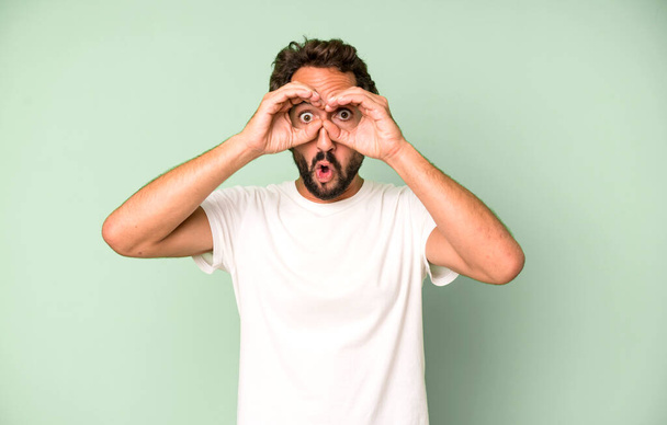 young crazy man feeling shocked, amazed and surprised, holding glasses with astonished, disbelieving look - Fotoğraf, Görsel