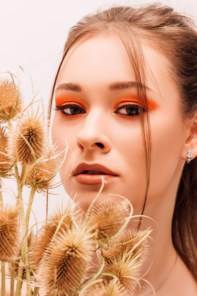 The girl holds dried flowers near her face. Portrait of a young beautiful girl with bright makeup and dried flowers - Photo, Image