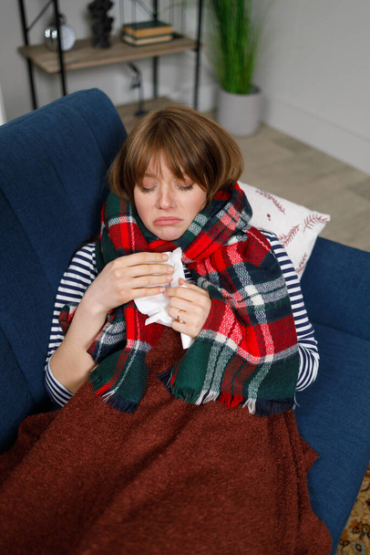 Donna malata con naso che cola sdraiata su un divano sotto una coperta con un fazzoletto - Foto, immagini