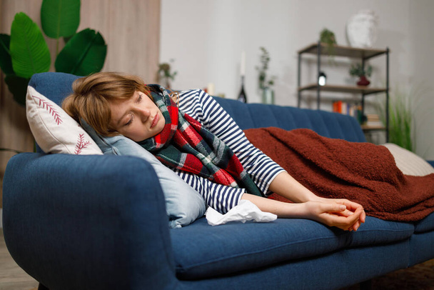 Femme malade avec la grippe ou un autre virus couvert d'une couverture dort sur le canapé à la maison - Photo, image