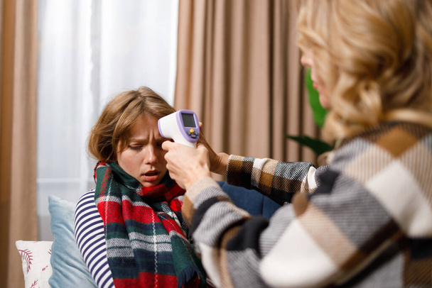 Madre mide temperatura con termómetro digital infrarrojo sin contacto de su hija enferma en casa - Foto, Imagen