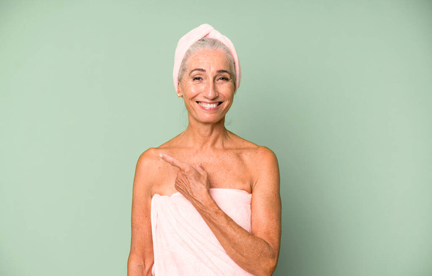 gray hair pretty woman smiling cheerfully, feeling happy and pointing to the side. wearing bathrobe and towel. beauty concept - Foto, afbeelding