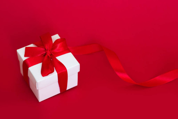 White box with a red ribbon on a red background. Greeting card concept - Foto, imagen