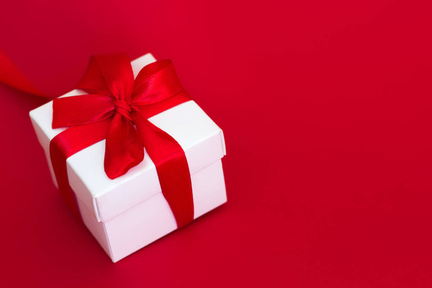 White box with a red ribbon on a red background, copy space. Greeting card concept - Fotó, kép