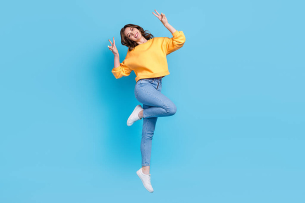 Full length photo of excited adorable girl dressed yellow pullover showing two v-signs jumping high isolated blue color background. - Fotografie, Obrázek