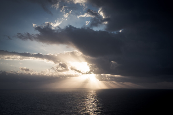 Dramática puesta de sol rayos a través de un cielo oscuro nublado sobre el océano. T
 - Foto, imagen