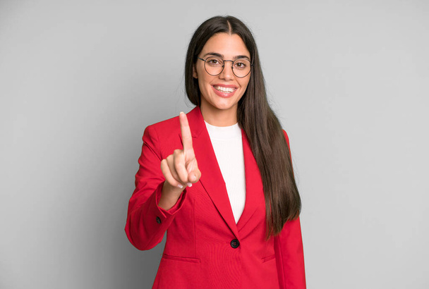 hispanic pretty woman smiling proudly and confidently making number one with red blazer. business concept - Valokuva, kuva