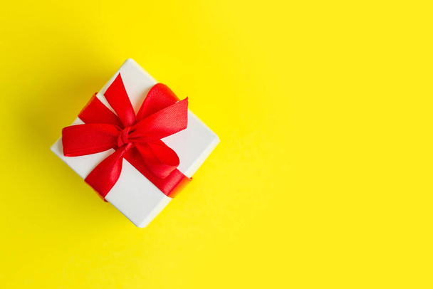White box with a red ribbon on a yellow background, copy space. Greeting card concept. Gift concept - Fotografie, Obrázek