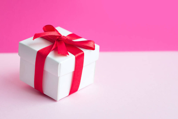 White box with a red ribbon on a light pink background, copy space. Greeting card concept. Sale concept - Foto, imagen