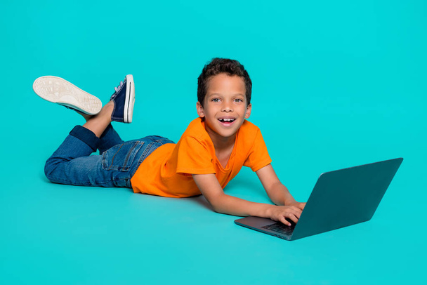 Foto de atractivo chico positivo acostado usando netbook juego de tiempo libre buen humor aislado sobre fondo de color cian. - Foto, Imagen