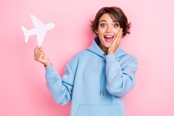 Portrait photo of young adorable pretty cute nice gorgeous woman wear blue hoodie hold paper white plane touch cheeks funny reaction isolated on pink color background. - Photo, Image