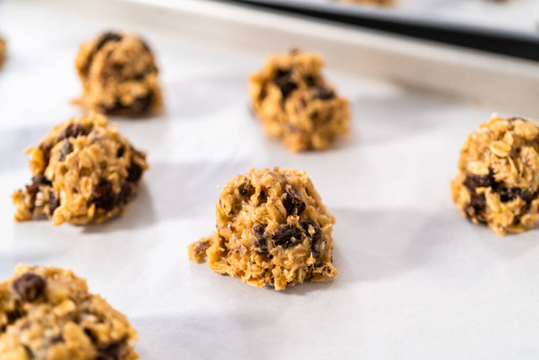 Scooping cookie dough with dough scoop into a baking sheet lined with parchment paper to bake soft oatmeal raisin walnut cookies. - Foto, Imagem