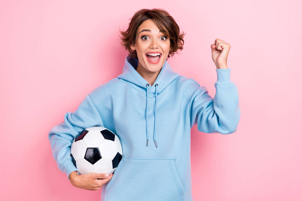 Portrait photo of young attractive gorgeous nice pretty woman wear blue hoodie fan sporty fist up celebrate hold football ball excited isolated on pink color background. - Φωτογραφία, εικόνα