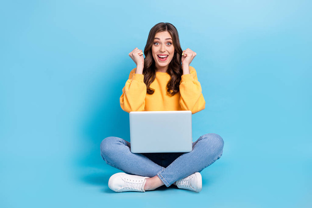 Full length photo of impressed lucky lady wear yellow sweater working modern device sitting legs crossed isolated blue color background. - Φωτογραφία, εικόνα