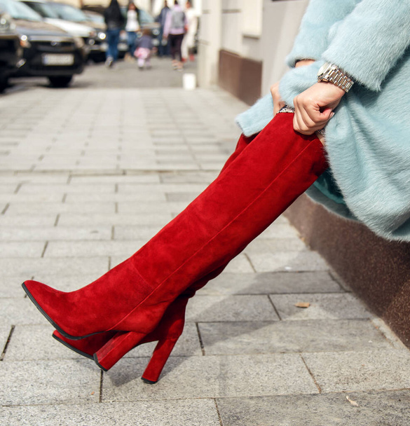 Una chica en botas de gamuza roja con tacones altos levanta sus zapatos en la calle. Zapatos y tacones de moda y con estilo. - Foto, Imagen