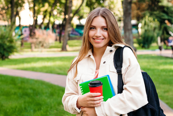 Студент блондинки гуляє в парку з блокнотом і чашкою кави, копіюючи простір. Концепція освіти
 - Фото, зображення