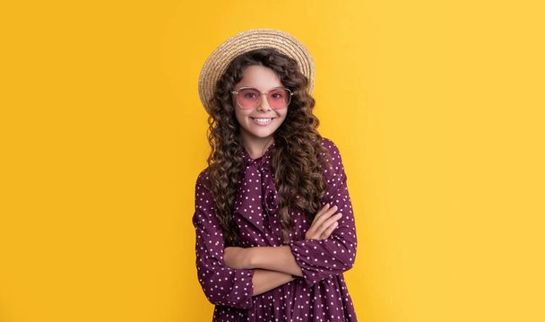 glad kid in straw hat and sunglasses with long brunette curly hair on yellow background. - 写真・画像