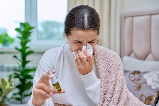 Flu season, autumn winter cold. Young teenage girl with runny nose treating rhinitis using nose drops spray. - Foto, afbeelding