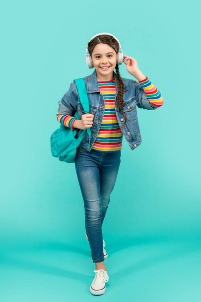 Happy teenage girl listening to music in headphones blue background, education. School education. Non-formal education. - Foto, Imagem