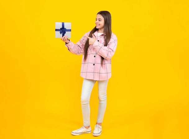 Portrait of a teenager child girl holding present box isolated over yellow studio background. Present, greeting and gifting concept. Birthday holiday concept - Photo, image
