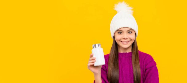 smiling child in winter hat with pill jar. food supplement. teen girl with natural pill products. Horizontal poster of isolated child face, banner header, copy space - Foto, Imagem