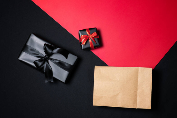 Top view of gift box with red, shopping paper bag, black ribbons and piggy bank isolated on red and black background. Shopping concept boxing day and black Friday sale composition. - Photo, Image