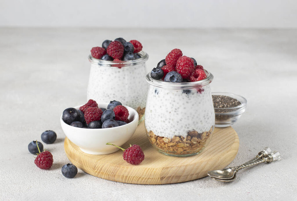 Chia pudding with muesli, fresh berries and natural yogurt on a wooden board on gray table. Healthy breakfast concept - Photo, image