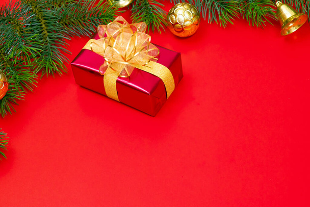クリスマスの背景概念。赤い背景にスプルースの枝と鐘を持つクリスマスギフトボックスの金のボールのトップビュー. - 写真・画像
