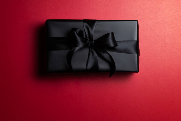 Top view of black christmas gift box with red and black ribbons isolated on red background. Shopping concept christmas day, valentin's day and black Friday sale composition. - Fotoğraf, Görsel