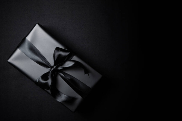 Top view of black gift box with black ribbons isolated on black background. Shopping concept boxing day and black Friday sale composition. - Valokuva, kuva