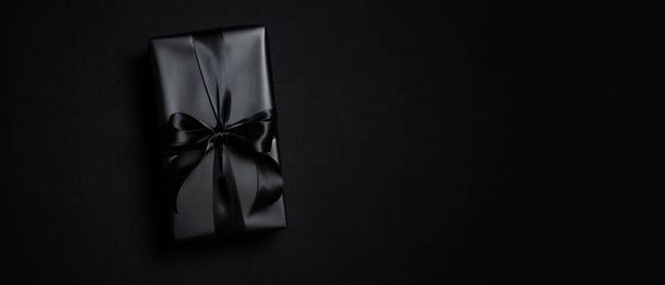 Top view of black gift box with black ribbons isolated on black background. Shopping concept boxing day and black Friday sale composition. - Fotografie, Obrázek