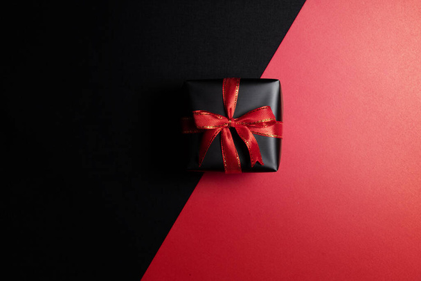 Top view of black gift box with red ribbon isolated on red and black background. Shopping concept boxing day and black Friday sale composition. - Valokuva, kuva