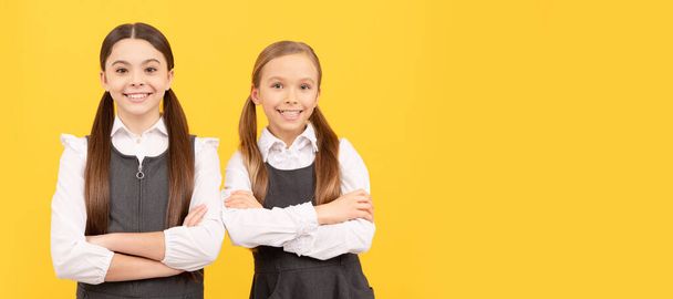 Школьные подружки. Счастливые дети носят школьную форму с перечеркнутыми руками на желтом фоне, 1 сентября. Горизонтальный изолированный плакат школьницы. Баннерный портрет школьницы - Фото, изображение