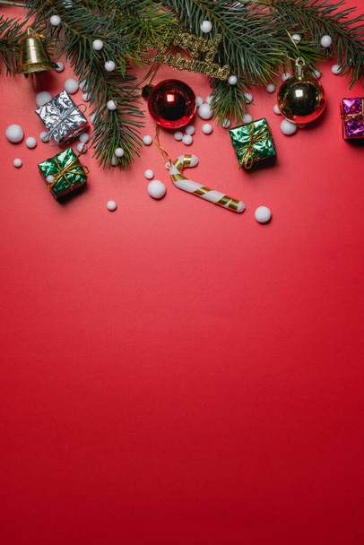 Christmas background concept. Top view of Christmas gift box colorful balls with spruce branches and bell on red background. - 写真・画像
